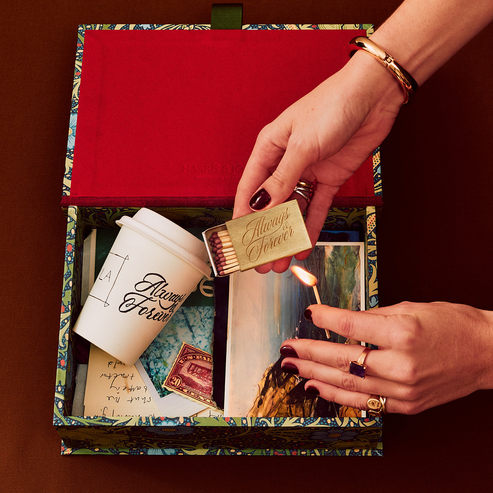 Person lighting a match inside a decorative box with a cup and other items.